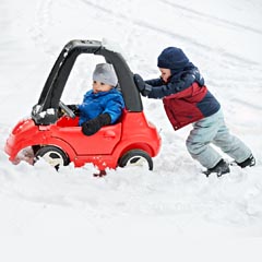 a boy pushing a girl in a toy car in the snow
